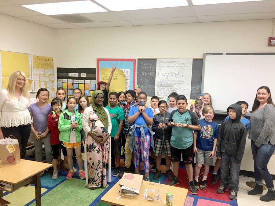 fourth grade students in a classroom smiling for the camera with a unitus branch employee on either end