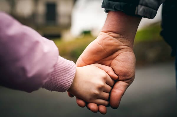 Dos formas de ahorrar dinero para una familia en crecimiento. Detalle de padre e hija cogidos de la mano.