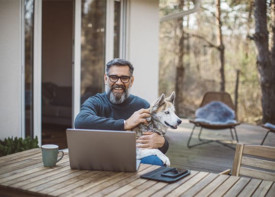 Un hombre sonriente chateando por vídeo en el patio trasero con su perro en brazos